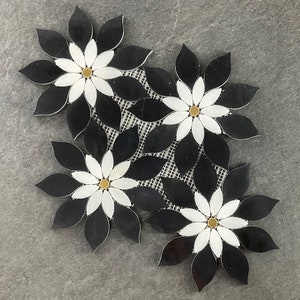 May include: Black and white mosaic tile with a floral design. The flowers have white petals and gold centers. The tiles are arranged in a cluster of four.