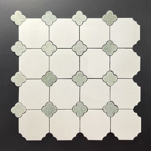 May include: A square tile mosaic featuring a grid pattern of white squares with light green clover-shaped accents. The clover shapes are connected by thin black lines, creating a decorative and geometric design. The tile has a smooth, clean finish.