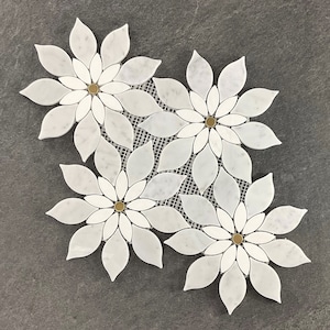 May include: Three white marble flower-shaped mosaic tiles with gold accents. Each tile is made up of individual marble pieces that are arranged in a flower shape. The tiles are set against a gray background.
