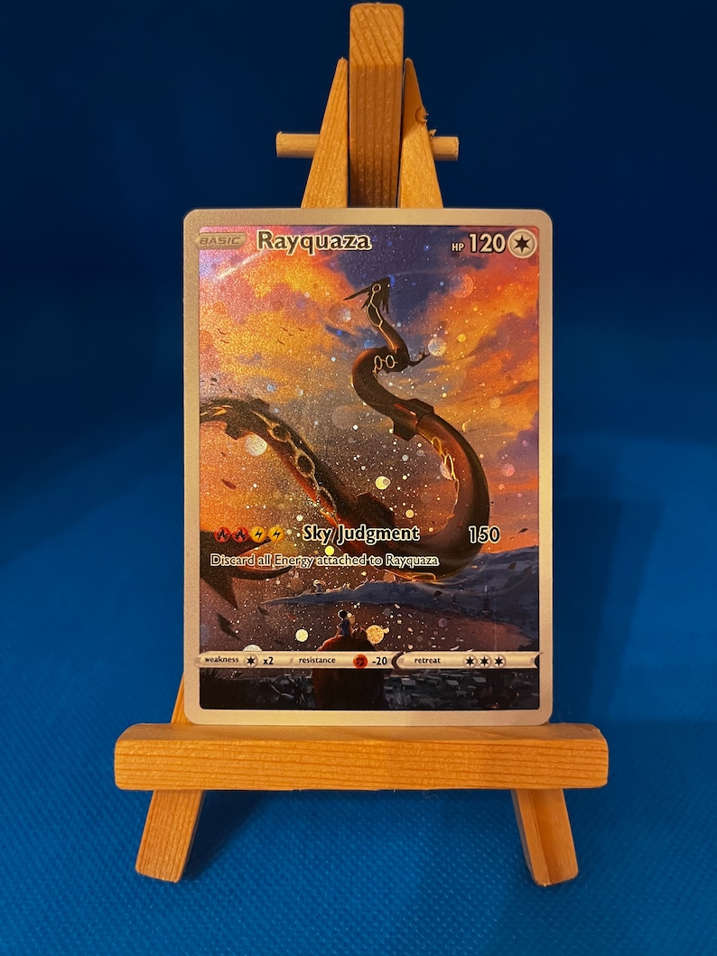 May include: A Pokemon trading card featuring Rayquaza, a green dragon-like creature with a gold chain around its neck. The card has a gold background with a sky and clouds. The card text reads "Sky Judgment: Discard all Energy attached to Rayquaza. 150".