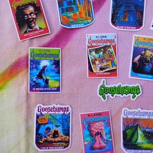 K&ouml;nnte beinhalten: Eine Sammlung farbenfroher Goosebumps-Aufkleber mit verschiedenen Buchcovern. Die Aufkleber zeigen Illustrationen von Monstern, Spukh&auml;usern und anderen gruseligen Bildern. Die Aufkleber tragen den Schriftzug "Goosebumps" und den Namen des Autors, R.L. Stine.
