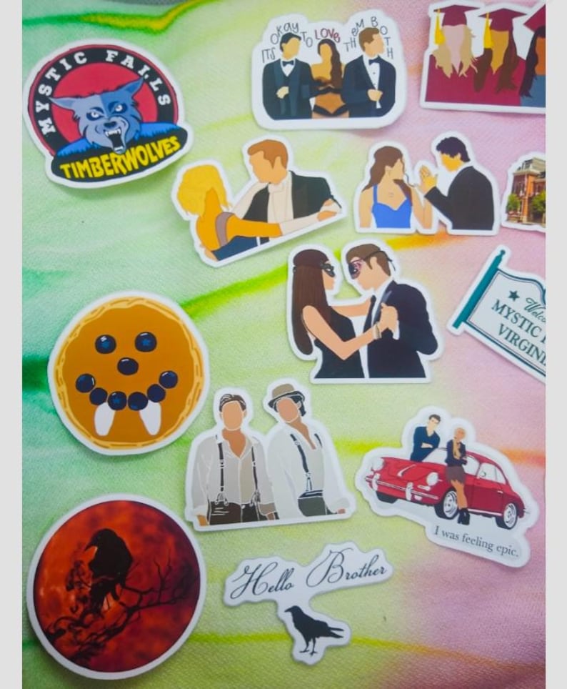 May include: A collection of stickers featuring various designs. Included are stickers with the text "Mystic Falls TimberWolves", a raven silhouette, and the phrase "Hello Brother". Other stickers depict cartoon figures and scenes.