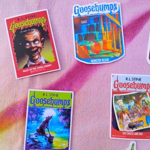 K&ouml;nnte beinhalten: Eine Sammlung farbenfroher Goosebumps-Aufkleber mit Buchcovern. Die Aufkleber zeigen Titel wie "Night of the Living Dummy", "Monster Blood", "The Werewolf of Fever Swamp" und "Say Cheese and Die!" auf einem rosa Hintergrund.