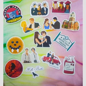 May include: A collection of colorful stickers featuring various designs. Included are stickers with the text "Mystic Falls Virginia", "Hello Brother", and "Mystic Falls Timber Wolves". Other stickers depict couples, a building, and a blood bag.