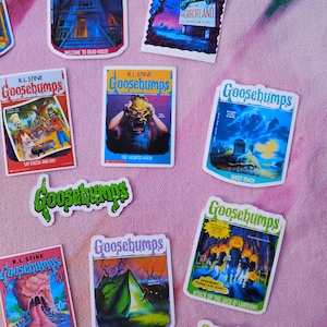 K&ouml;nnte beinhalten: Eine Sammlung farbenfroher Goosebumps-Aufkleber mit verschiedenen Buchcovern. Die Aufkleber zeigen gruselige Illustrationen und Titel wie "Welcome to Dead House", "Horrorland" und "The Haunted Mask". Die Aufkleber befinden sich auf einer rosa Oberfl&auml;che.