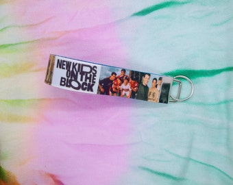 Könnte beinhalten: Ein New Kids on the Block Schlüsselanhänger mit einem Gruppenfoto der Bandmitglieder. Der Schlüsselanhänger hat einen blauen Hintergrund mit dem Namen der Band in weißem Text. Ein silberfarbener Metallring ist angebracht.