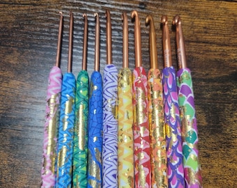 May include: Set of ten colorful crochet hooks with gold accents. Each hook has a different pattern and color, including pink, blue, green, and yellow.