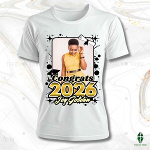 May include: White t-shirt featuring a graduation-themed design. The design includes a photo of a person in a yellow dress, the words "Congrats 2026" in gold, and the name "Joy Golden". The design is framed with black accents.