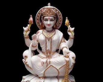 May include: White marble statue of a Hindu goddess sitting on a lotus throne. She is adorned with gold jewelry and has a serene expression.