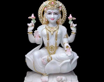 May include: White marble statue of the Hindu goddess Lakshmi, seated on a lotus flower with a white mouse at her feet. She is adorned with gold jewelry and holds a lotus flower in each hand.