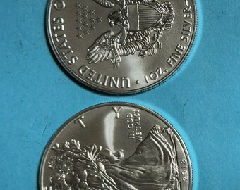 May include: Two silver American Eagle coins, one with the American bald eagle and the words "United States of America, One Ounce, Fine Silver", and the other with the Statue of Liberty and the words "In God We Trust, Liberty, 2018".
