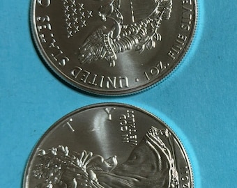 May include: Two silver American Eagle coins, one with the front side showing a bald eagle with outstretched wings and the words "United States of America, One Dollar", and the other with the back side showing a woman holding a torch and the words "In God We Trust, Liberty, 2012".