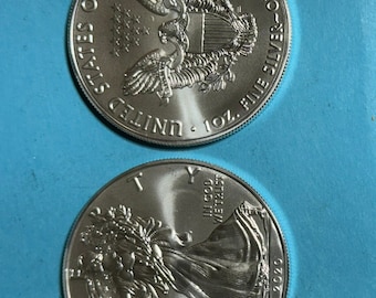 May include: Two silver American Eagle coins, one with the bald eagle and the words "United States of America, 1 oz. Fine Silver - One Dollar", and the other with Lady Liberty and the words "In God We Trust, 2020".