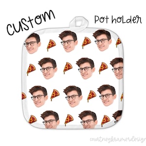 May include: White pot holder with a repeating pattern of a person's face and a slice of pizza. The text "CUSTOM" is in the upper left corner and "pot holder" is in the upper right corner.
