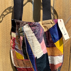 Könnte beinhalten: Eine Patchwork-Tragetasche mit schwarzem Riemen. Die Tasche besteht aus verschiedenen Stoffresten in verschiedenen Farben, darunter Blau, Gelb, Rosa und Braun. Ein Etikett mit der Nummer 1 ist angebracht.
