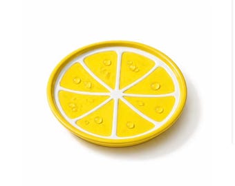 Könnte beinhalten: Ein gelber Keramikuntersetzer in Form einer Zitronenscheibe. Der Untersetzer hat eine leuchtend gelbe Innenseite mit weißen Segmenten und einen gelben Rand. Kleine, klare, tröpfchenförmige Details sind auf der Oberfläche verteilt.