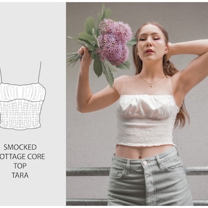 May include: A white smocked crop top with thin straps. The top has a gathered, ruffled neckline and a fitted bodice. The text "SMOCKED COTTAGE CORE TOP TARA" is printed below the image of the top.