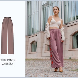 May include: A woman wearing a white crop top and a long, flowing pair of silky pants with a floral design. The pants are a light pink color and have a wide leg. The woman is standing in front of a building with large windows.