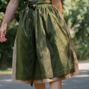 May include: A green dirndl skirt with a brown bodice and white blouse. The skirt has a brown ribbon tied around the waist and a white polka dot pattern on the bottom.