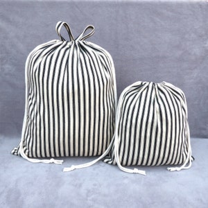 May include: Two striped drawstring bags, one larger than the other. Both bags are made of white fabric with black stripes and have white drawstrings.
