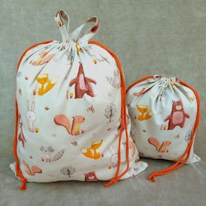May include: Two drawstring bags with orange trim and a white background. The bags are printed with a pattern of woodland animals, including foxes, squirrels, bears, and rabbits.