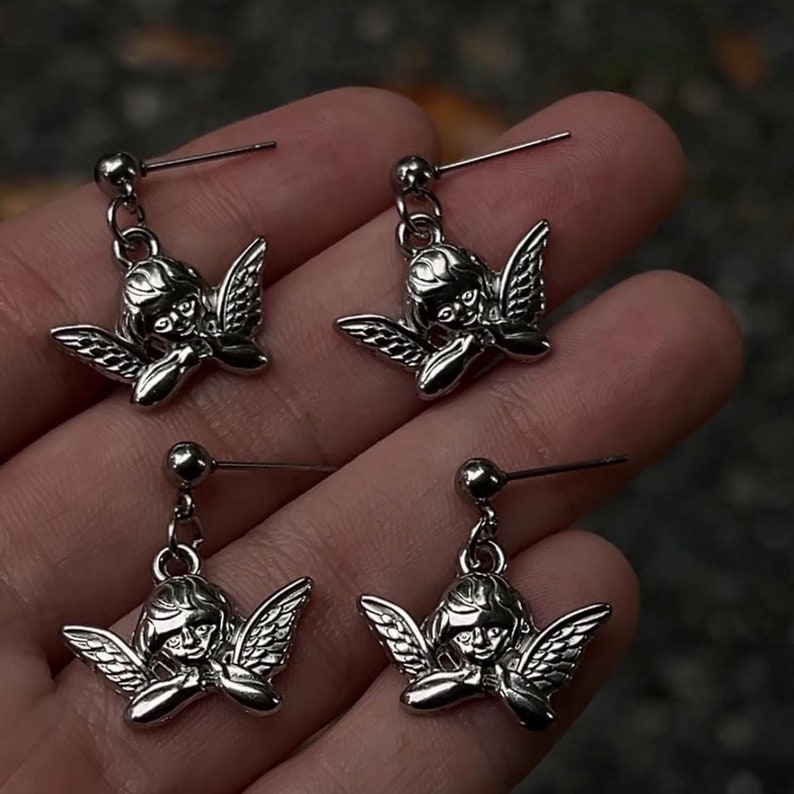Peut inclure: Une paire de boucles d'oreilles pendantes argent&eacute;es avec un motif de ch&eacute;rubin ail&eacute;. Les boucles d'oreilles sont sur un fond blanc.