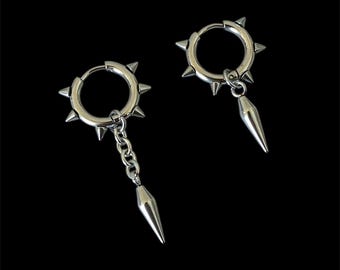 May include: A pair of silver hoop earrings with spikes and a dangling spike charm. The earrings are made of metal and have a punk rock aesthetic.