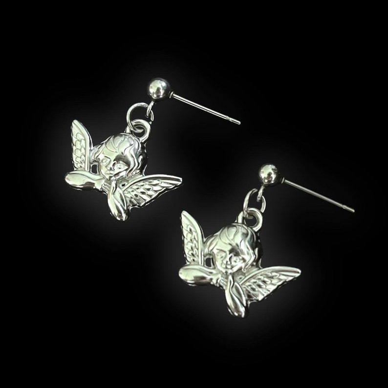 Peut inclure: Une paire de boucles d'oreilles en argent avec un motif de ch&eacute;rubin. Chaque boucle d'oreille a une petite boule d'argent en haut et un charme de ch&eacute;rubin d&eacute;taill&eacute; suspendu en dessous.