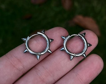 May include: A pair of silver hoop earrings with pointed spikes around the edge.