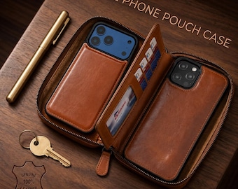 May include: A brown leather zippered 2 PHONE POUCH CASE containing two smartphones, multiple card slots, and a clear ID window. A gold-toned pen and a metal key are placed nearby. The leather case features a stamped logo reading GENUINE 100% LEATHER.
