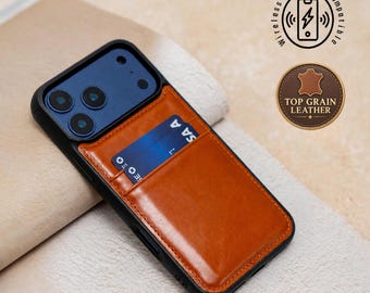 Puede incluir: Una funda de smartphone negra con un tarjetero de cuero marrón claro adherido a la parte posterior, que contiene una tarjeta azul. La funda tiene un recorte para la cámara e iconos con el texto Wireless Charging Compatible y Top Grain Leather.