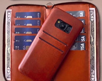 Puede incluir: Una cartera de cuero marrón con una correa de muñeca a juego. La cartera está abierta, revelando ranuras para tarjetas, efectivo y una funda de teléfono marrón. Se ven tarjetas de crédito y billetes de 50 euros.