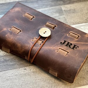 Puede incluir: Un diario de cuero marr&oacute;n con cierre de bot&oacute;n de madera y las iniciales "JRF" grabadas en la portada.