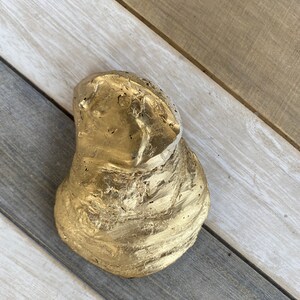 May include: A gold-painted, irregularly shaped rock with a rough, textured surface. The rock is a natural object that has been painted gold.