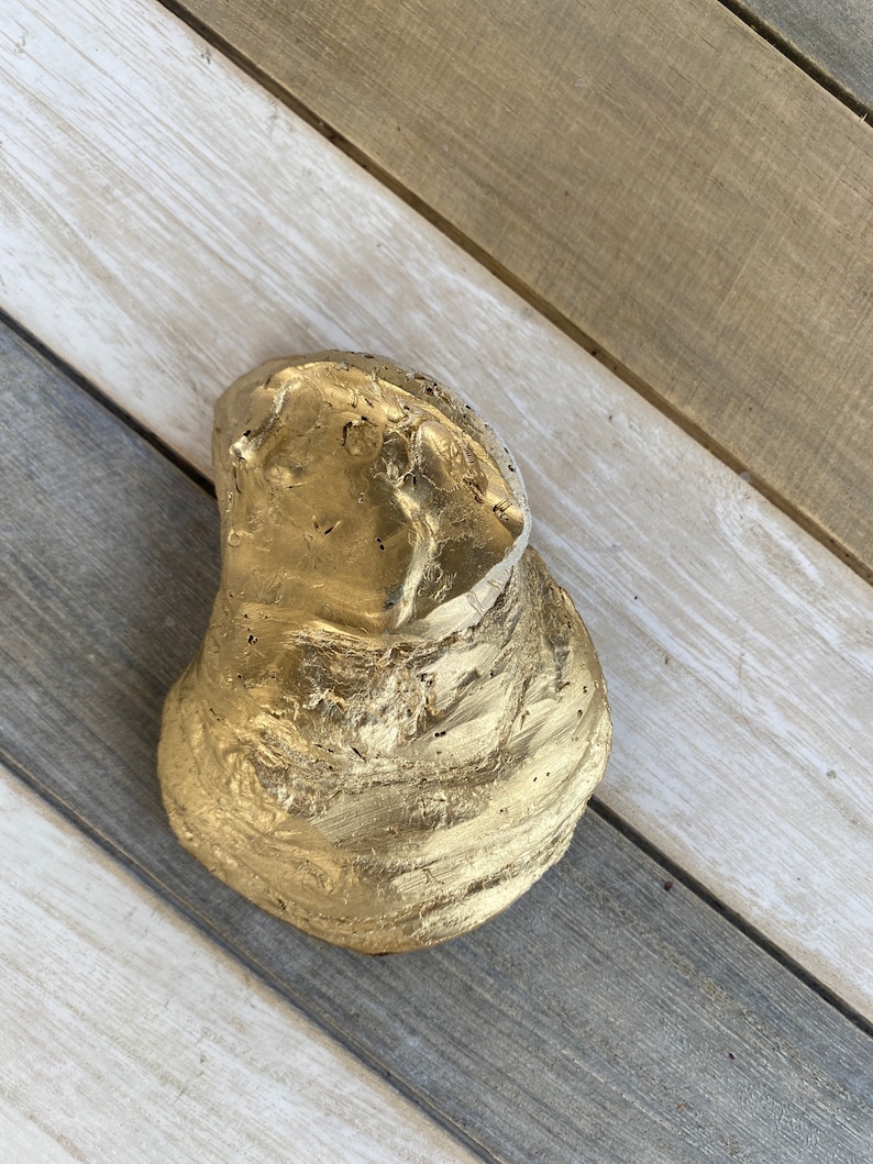 May include: A gold-painted, irregularly shaped rock with a rough, textured surface. The rock is a natural object that has been painted gold.