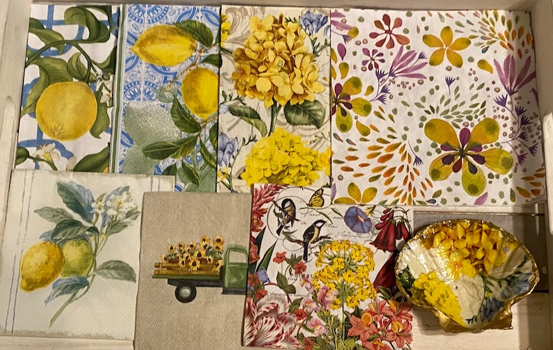 May include: A collection of eight decorative paper napkins with various floral and lemon designs. The napkins feature yellow, green, white, red, and purple colors. The napkins are arranged in a collage on a white surface.