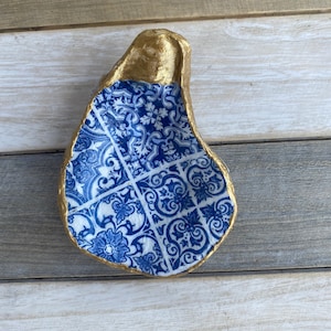 May include: A blue and white patterned oyster shell dish with a gold rim. The dish is made of concrete and is perfect for holding jewelry or other small items.