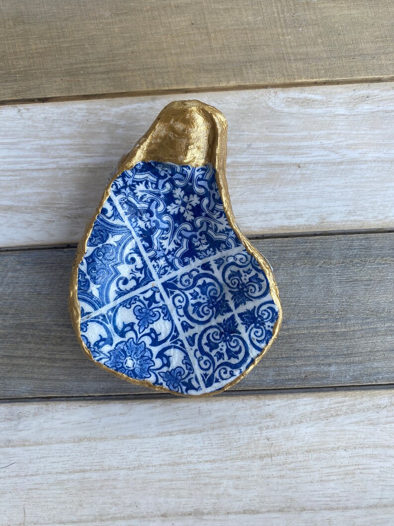 May include: A blue and white patterned oyster shell dish with a gold rim. The dish is made of concrete and is perfect for holding jewelry or other small items.