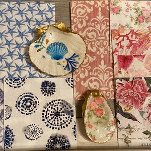 May include: A collection of decorative napkins with various patterns, including blue starfish, anchors, fish, and circles. Two decorative seashell dishes are included, one with a blue and white floral design and the other with a pink floral design.