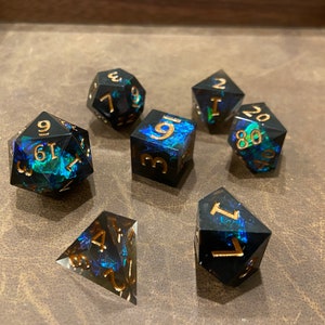 May include: A set of iridescent black dice with gold numbers. The dice are a d4, d6, d8, d10, d12, and d20. The dice are on a brown leather surface.