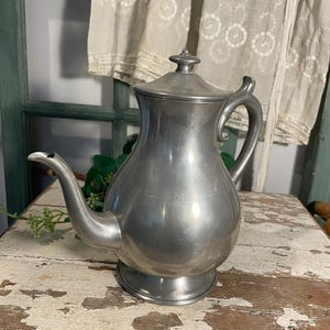 May include: A silver pewter teapot with a rounded body and a lid. The teapot has a spout and a handle. The teapot is sitting on a wooden surface.