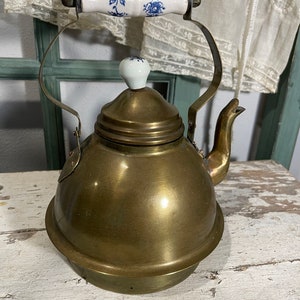 May include: A brass teapot with a white porcelain lid and handle. The handle has a blue and white floral design.
