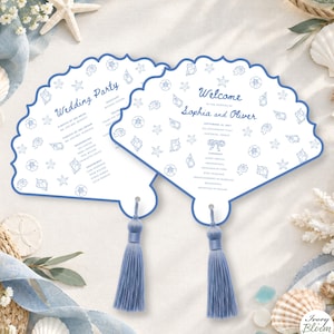 May include: Two shell-shaped wedding program fans with blue ink text and illustrations of seashells and starfish. Each fan features a blue tassel at the base. The text includes "Welcome to the wedding of Sophia and Oliver" and "Wedding Party".