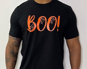 May include: Black t-shirt with the word "BOO!" in orange, featuring spiderwebs in the letters. The shirt is short-sleeved and has a crew neck. The design is centered on the chest.
