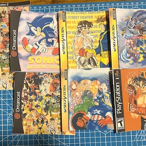 May include: A collection of video game cases featuring various characters and titles, including Sonic Adventure, Tekken 3, Street Fighter, and Marvel characters. The cases are all in different colors and styles, and some have text on them.