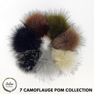 May include: A collection of seven faux fur pom poms in various camouflage colors, including black, brown, gray, green, and white. The pom poms are arranged in a circle on a white background.