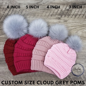 May include: Four knitted hats with faux fur pom-poms in various sizes: 6 inches, 5 inches, 4 inches, and 3 inches. The hats are in shades of pink, red, and beige.
