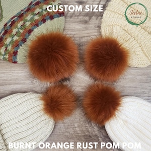 May include: Four burnt orange rust pom poms are displayed with knitted hats. The pom poms are fluffy and round, with a rich, warm color. The hats are cream and green, with the text "CUSTOM SIZE" and "BURNT ORANGE RUST POM POM" visible.