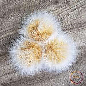 May include: Three fluffy pom poms in shades of white and yellow. The pom poms are made of faux fur and are perfect for adding a touch of whimsy to any project.