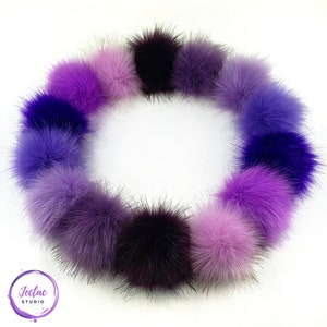 May include: A circle of 15 purple and lavender faux fur pom poms. The pom poms are arranged in a gradient from dark purple to light lavender.
